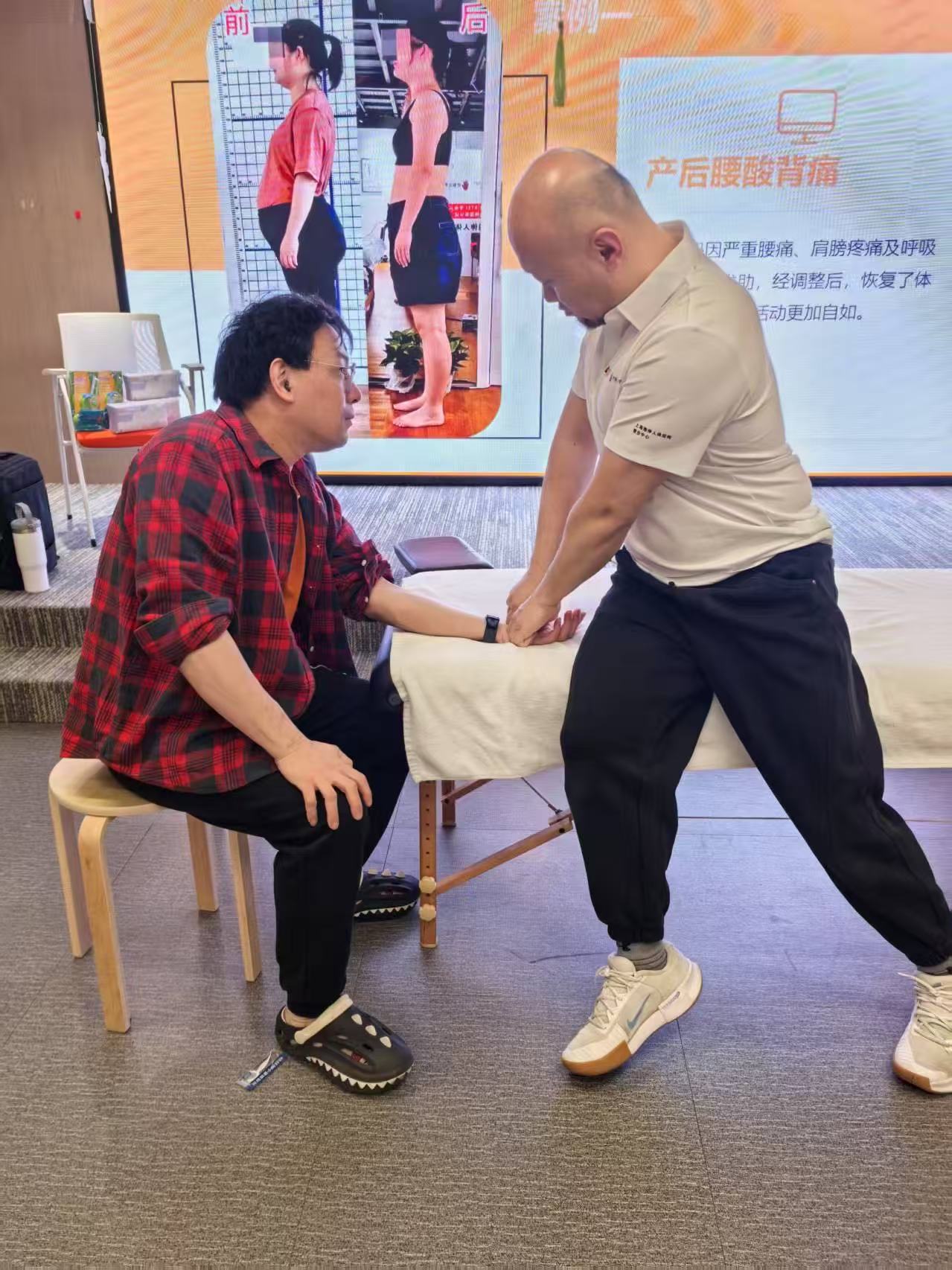 课程现场，参与者坐在凳子上，Frank在其手腕附近演示手法
