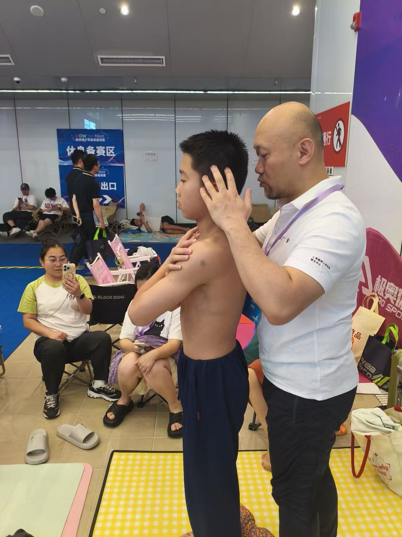 Frank张伟在游泳赛事现场观察并引导一名青少年运动者的上肢动作
